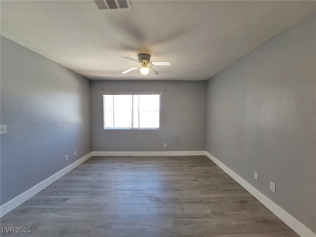 spare room featuring visible vents, baseboards, wood finished floors, and a ceiling fan