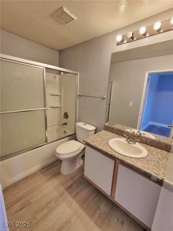 full bath featuring visible vents, a textured ceiling, wood finished floors, bath / shower combo with glass door, and vanity