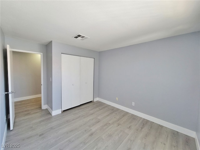 unfurnished bedroom with light wood-type flooring, visible vents, baseboards, and a closet