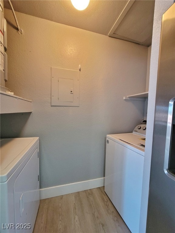 laundry room with light wood-style flooring, electric panel, baseboards, laundry area, and washing machine and clothes dryer