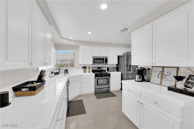 kitchen featuring recessed lighting, stainless steel appliances, tile counters, and white cabinetry