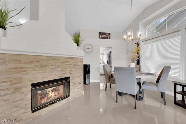 dining space featuring baseboards, a chandelier, a fireplace, and vaulted ceiling