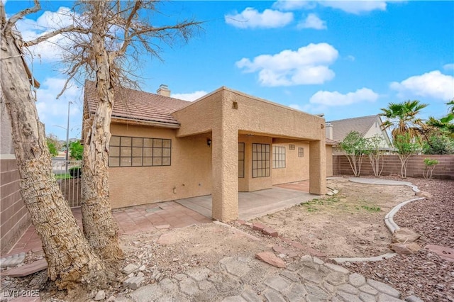 rear view of property with a patio area, stucco siding, a chimney, and fence