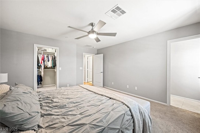 bedroom with a spacious closet, visible vents, light carpet, a closet, and a ceiling fan