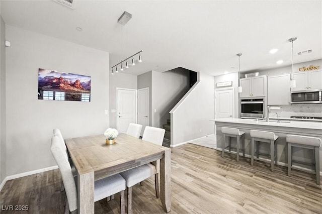 dining room featuring visible vents, light wood-style floors, rail lighting, baseboards, and stairs