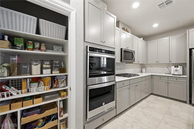 kitchen featuring visible vents, backsplash, gray cabinetry, light countertops, and stainless steel appliances