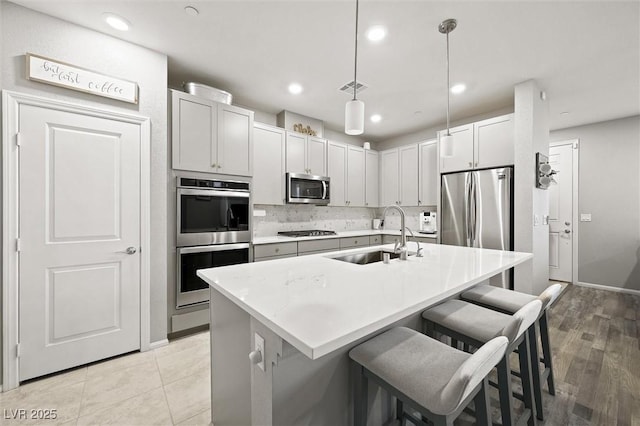 kitchen with a sink, a kitchen breakfast bar, tasteful backsplash, stainless steel appliances, and light countertops