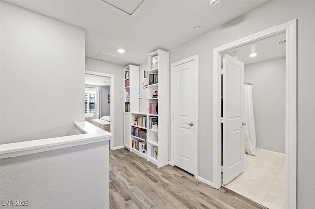 hallway with baseboards, attic access, and light wood-style flooring