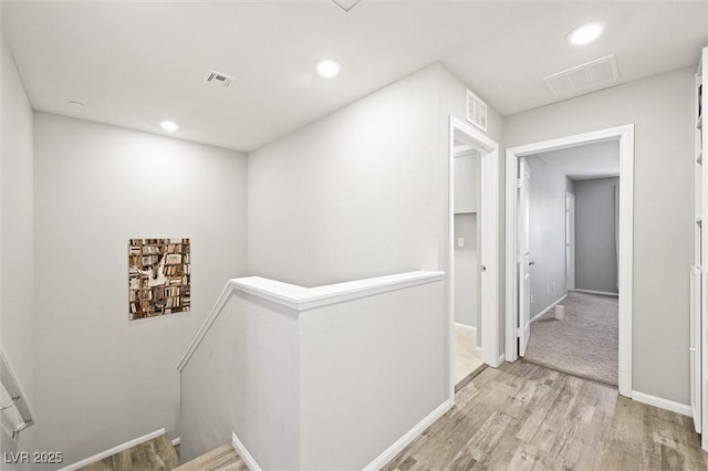 hall with visible vents, an upstairs landing, and light wood-style floors