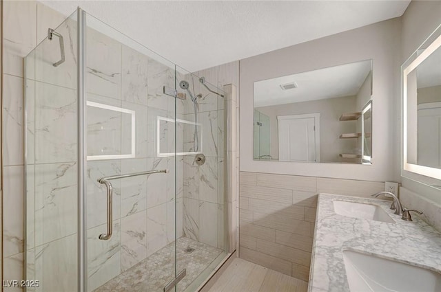 bathroom with a sink, a marble finish shower, and tile walls