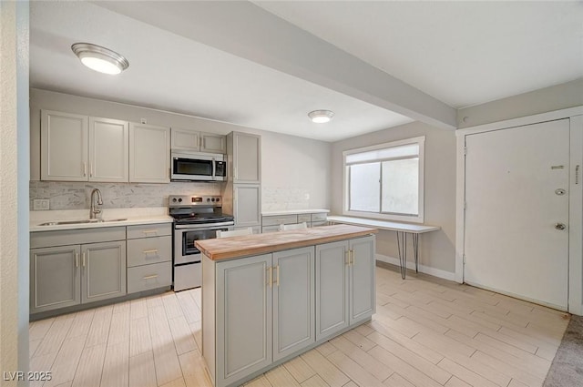 kitchen with gray cabinets, a sink, butcher block countertops, stainless steel appliances, and tasteful backsplash