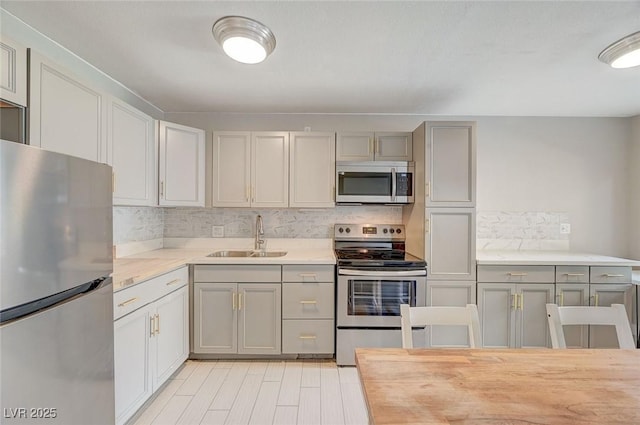 kitchen featuring light countertops, decorative backsplash, gray cabinets, stainless steel appliances, and a sink