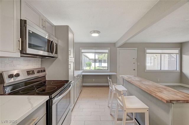 kitchen featuring baseboards, gray cabinets, butcher block countertops, stainless steel appliances, and backsplash