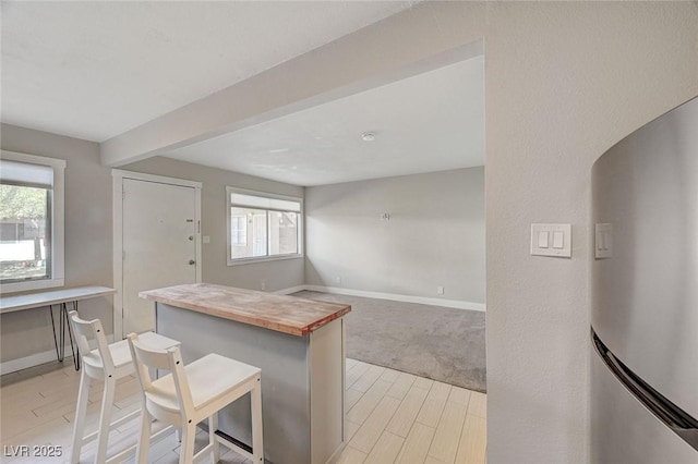 kitchen featuring baseboards, butcher block counters, a kitchen breakfast bar, freestanding refrigerator, and light wood-style floors