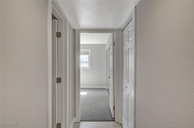 hallway featuring light carpet and a textured wall