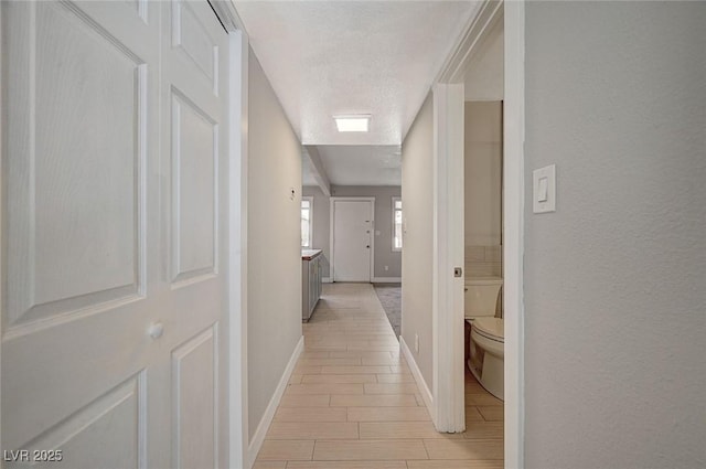 hall with a textured ceiling, baseboards, and wood tiled floor