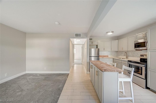 kitchen with a kitchen island, a breakfast bar, a sink, stainless steel appliances, and tasteful backsplash