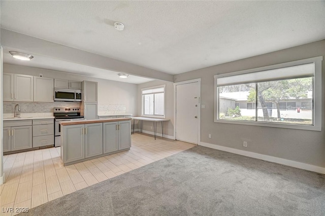 kitchen featuring a kitchen island, light carpet, gray cabinets, appliances with stainless steel finishes, and a sink