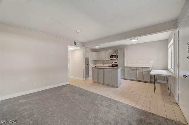 kitchen featuring visible vents, a kitchen island, gray cabinets, decorative backsplash, and appliances with stainless steel finishes