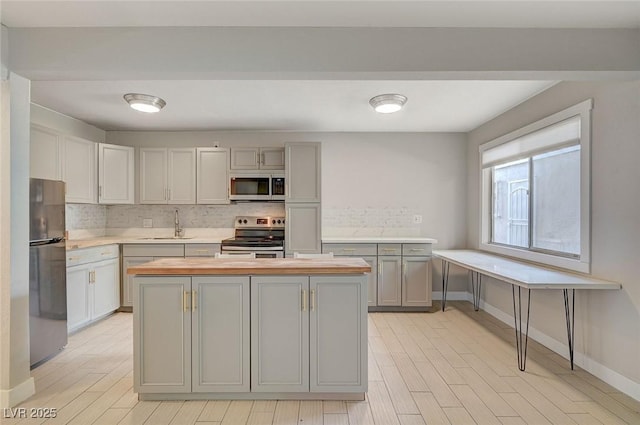 kitchen featuring gray cabinetry, a center island, stainless steel appliances, butcher block counters, and decorative backsplash