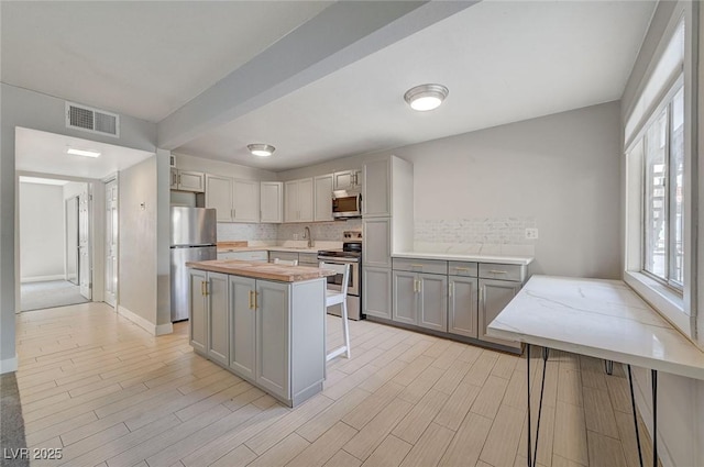 kitchen featuring visible vents, gray cabinets, a sink, appliances with stainless steel finishes, and decorative backsplash