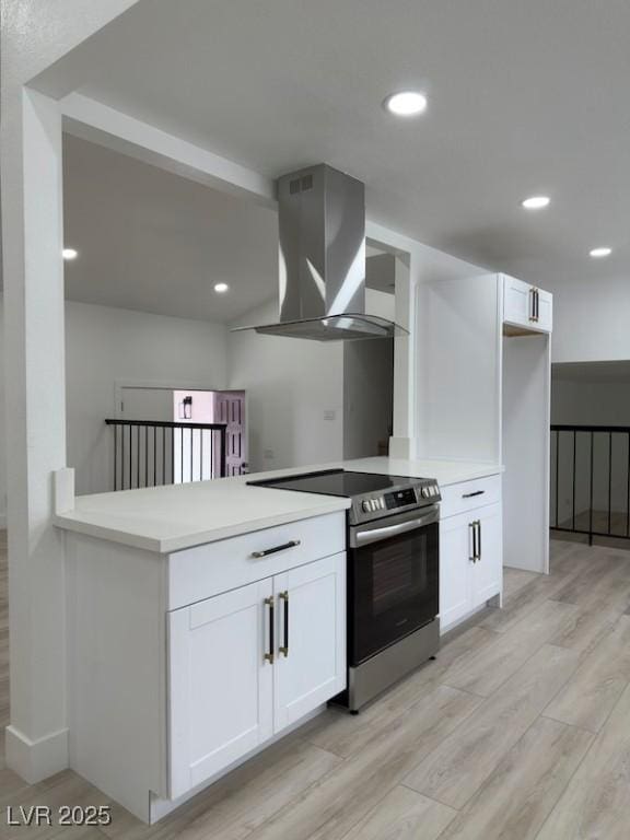 kitchen with stainless steel electric stove, white cabinets, and wall chimney range hood