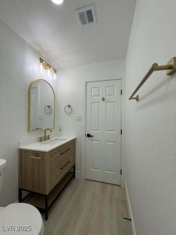 half bathroom with visible vents, baseboards, toilet, wood finished floors, and vanity