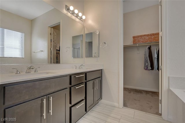 bathroom featuring a walk in closet, double vanity, baseboards, and a sink