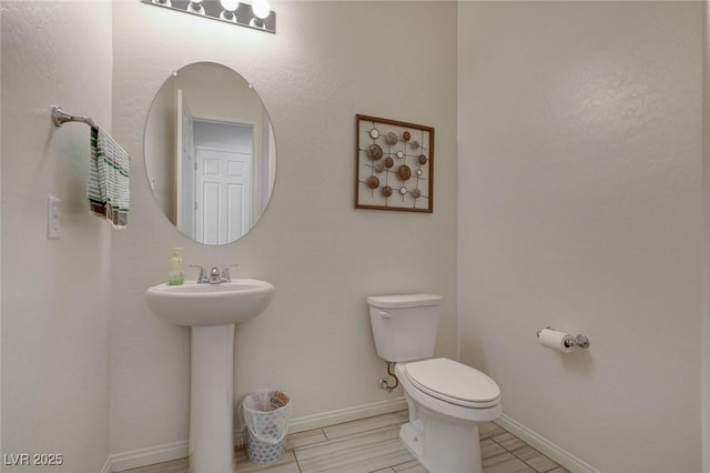 half bathroom featuring a sink, baseboards, and toilet