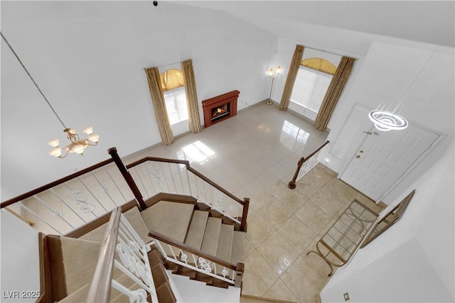 interior space with an inviting chandelier, stairway, a warm lit fireplace, and high vaulted ceiling