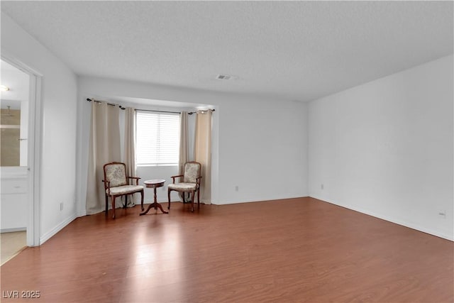 living area with wood finished floors, visible vents, and a textured ceiling