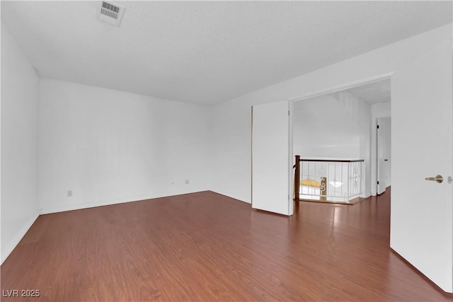 empty room featuring wood finished floors, visible vents, and a textured ceiling