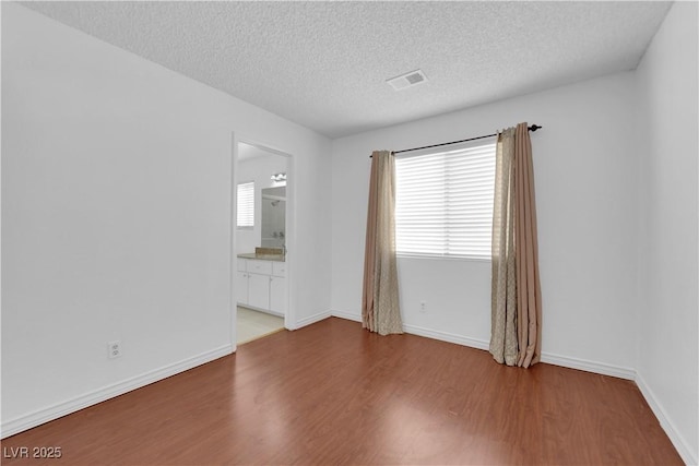 unfurnished room with baseboards, wood finished floors, visible vents, and a textured ceiling