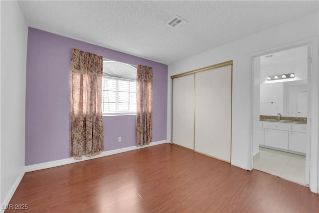 unfurnished bedroom featuring visible vents, a textured ceiling, a closet, light wood-style floors, and baseboards