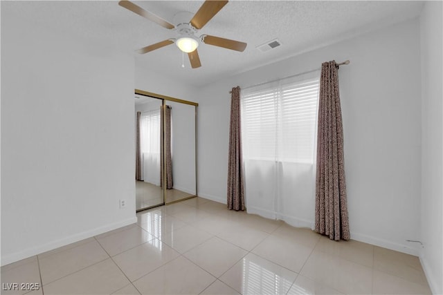 spare room featuring tile patterned floors, visible vents, a ceiling fan, a textured ceiling, and baseboards