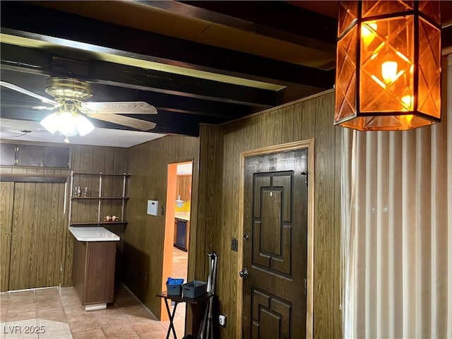 foyer with light tile patterned floors, beamed ceiling, wooden walls, and ceiling fan