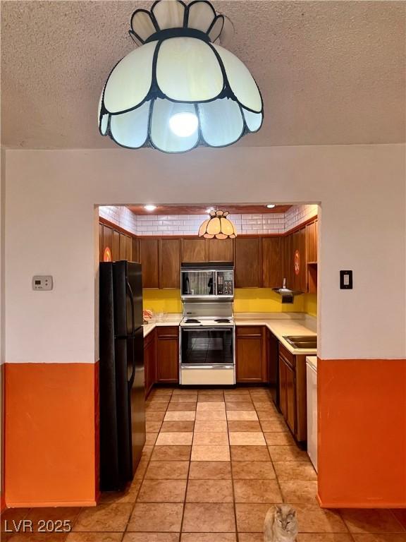 kitchen with light tile patterned floors, black appliances, light countertops, a textured ceiling, and brown cabinets