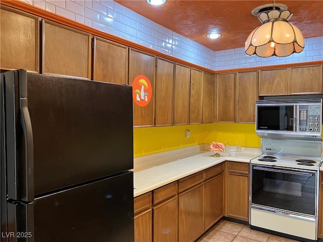 kitchen featuring stainless steel microwave, light countertops, light tile patterned floors, freestanding refrigerator, and electric stove