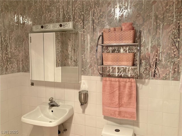 bathroom featuring a sink, a wainscoted wall, and wallpapered walls