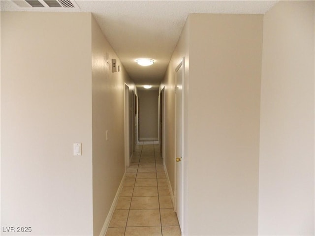 corridor featuring light tile patterned floors, visible vents, a textured ceiling, and baseboards