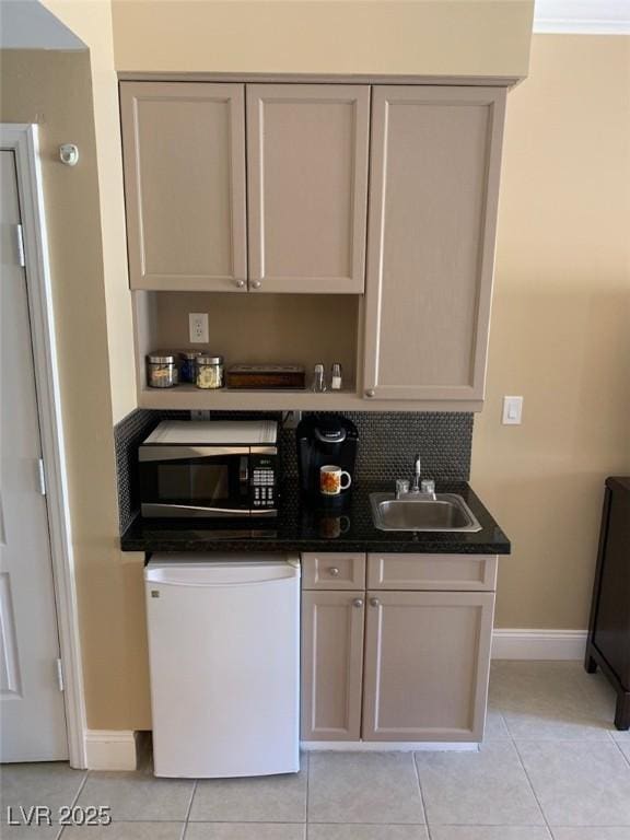 kitchen with a sink, stainless steel microwave, dark countertops, fridge, and light tile patterned floors