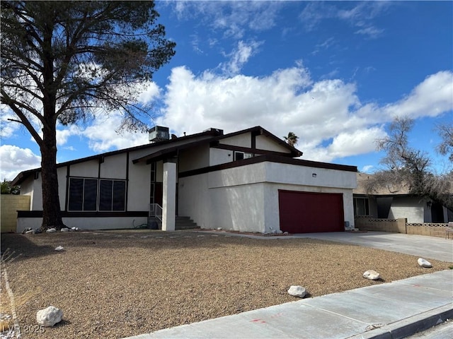 view of front facade featuring stucco siding, concrete driveway, an attached garage, and fence