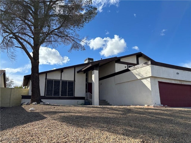 view of front of home with stucco siding, an attached garage, gravel driveway, and fence