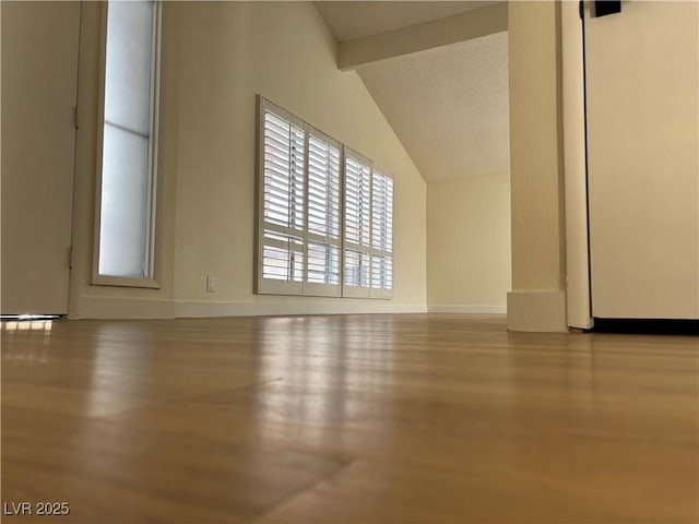 interior space with vaulted ceiling with beams, wood finished floors, and baseboards