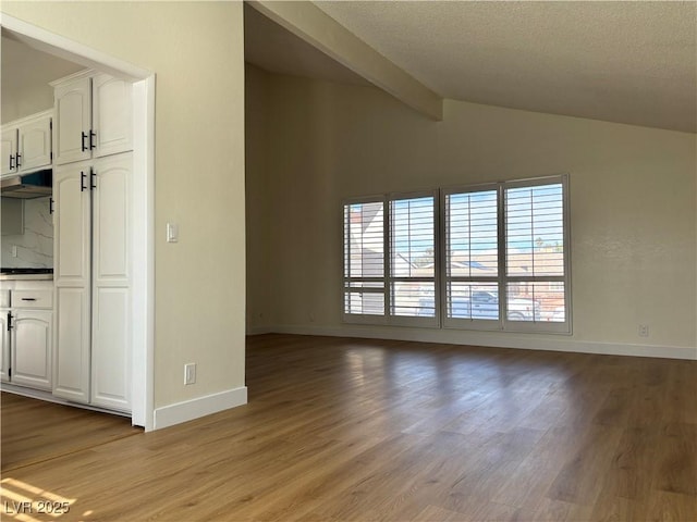 unfurnished living room with lofted ceiling with beams, baseboards, light wood-type flooring, and a textured ceiling