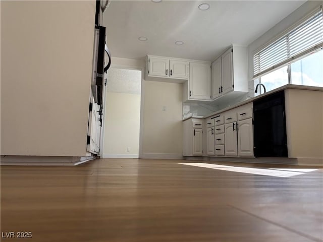 kitchen with light wood finished floors, black dishwasher, white cabinets, light countertops, and baseboards