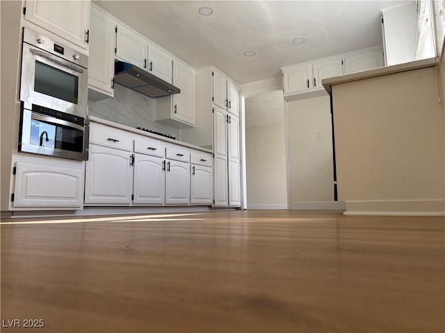 kitchen with backsplash, baseboards, under cabinet range hood, double oven, and white cabinets