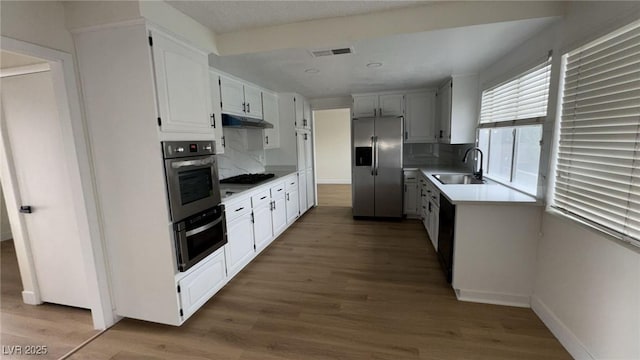 kitchen with wood finished floors, visible vents, a sink, black appliances, and under cabinet range hood