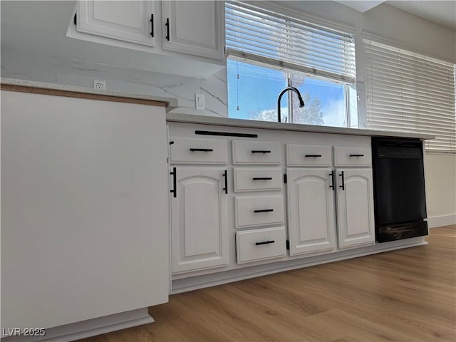 kitchen featuring a sink, white cabinets, light wood-type flooring, and light stone countertops