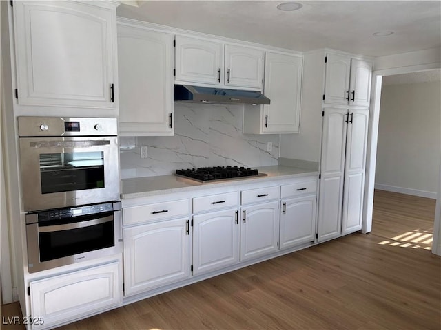 kitchen featuring under cabinet range hood, gas cooktop, stainless steel double oven, and light wood-style flooring